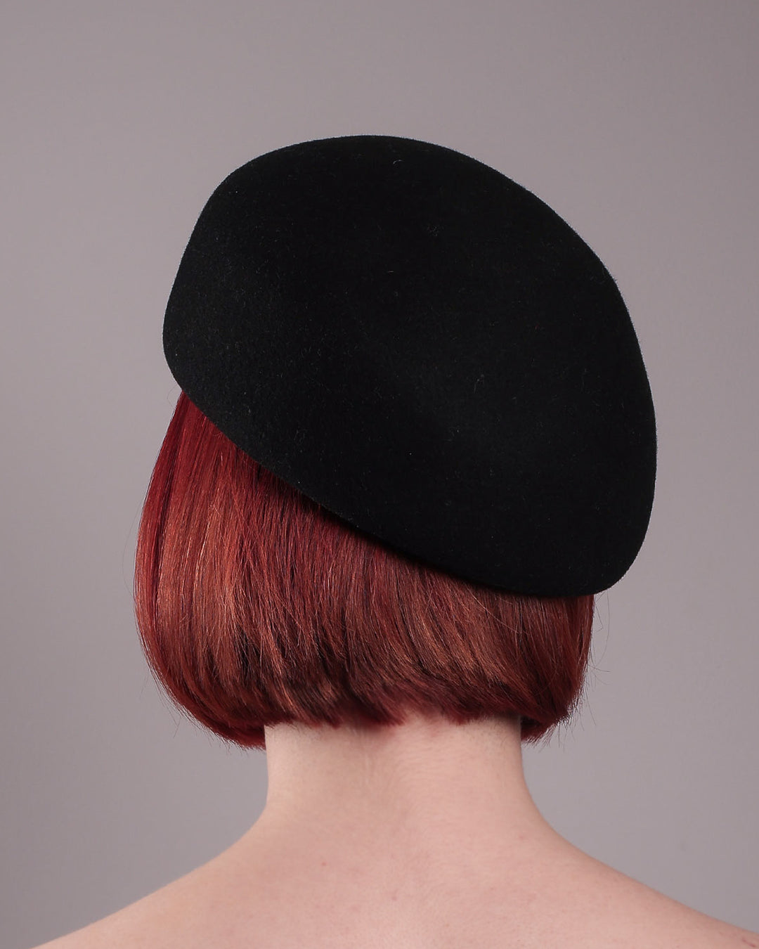 The female model is showcasing the back of the wool beret-style hat. The black hat is decorated with a real gold-plated brass metal branch motif adorned with crystal-tipped buds. The side beret is higher on the left side and shorter on the right side, and is suggested to be worn tilted. Designed by Merve Bayindir.