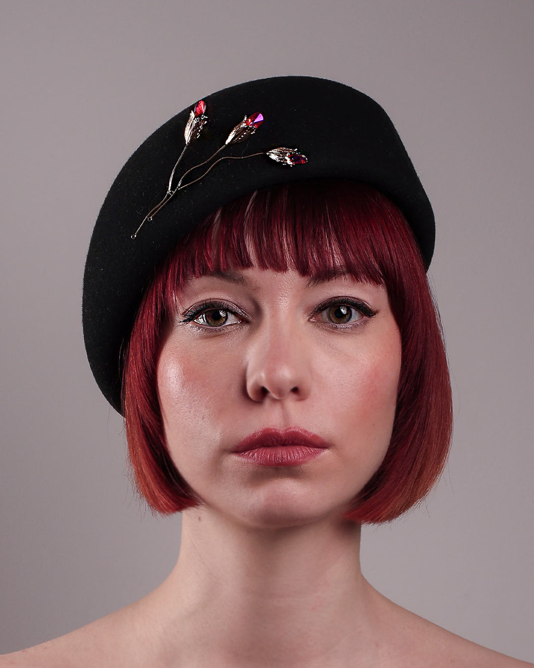 The female model is showcasing the front close up view of the wool beret-style hat. The black hat is decorated with a real gold-plated brass metal branch motif adorned with crystal-tipped buds. The side beret is higher on the left side and shorter on the right side, and is suggested to be worn tilted. Designed by Merve Bayindir.