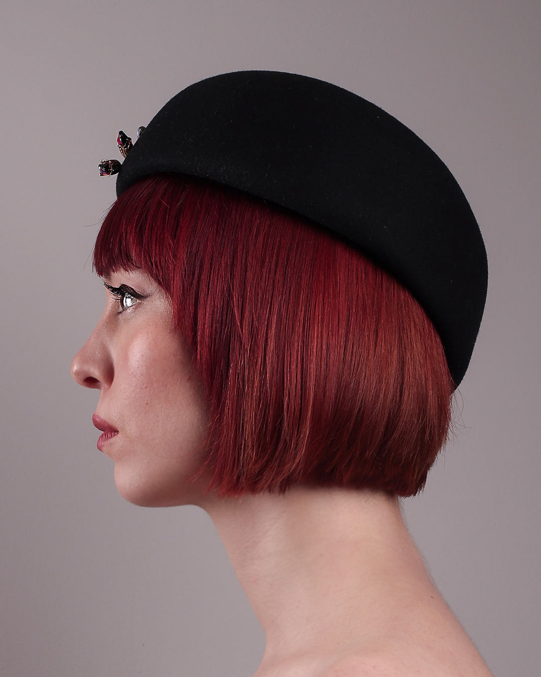 The female model is showcasing the left side close up view of the wool beret-style hat. The black hat is decorated with a real gold-plated brass metal branch motif adorned with crystal-tipped buds. The side beret is higher on the left side and shorter on the right side, and is suggested to be worn tilted. Designed by Merve Bayindir.