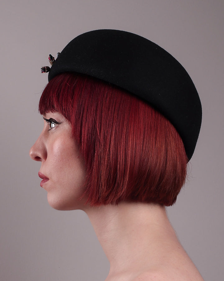 The female model is showcasing the left side close up view of the wool beret-style hat. The black hat is decorated with a real gold-plated brass metal branch motif adorned with crystal-tipped buds. The side beret is higher on the left side and shorter on the right side, and is suggested to be worn tilted. Designed by Merve Bayindir.