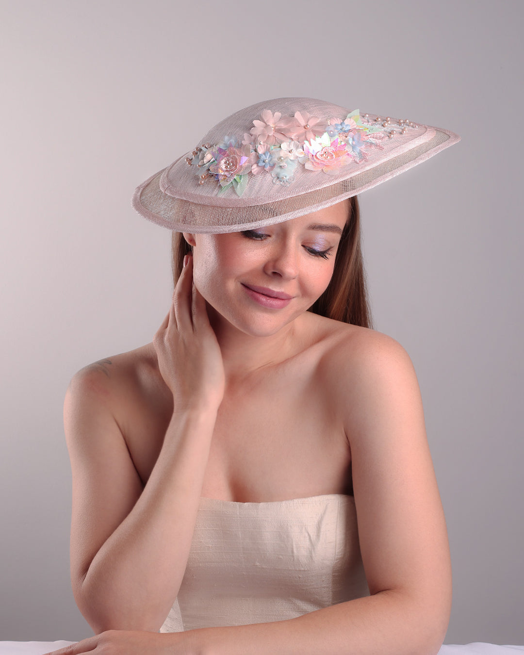 The model is showcasing the front the asymetric tear-drop shaped layered pink saucer hat which has two layers of grey in the bottom and topped with a two layer pink colour of same style saucer in a smaller size. The top of the pink layer, hat is decorated with a 3D lace embroiderey embellished with silk flowers, pearls beads and sequins.