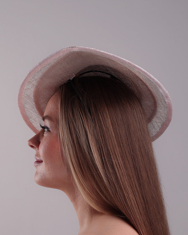 The model is showcasing the left side of the asymetric tear-drop shaped layered pink saucer hat which has two layers of grey in the bottom and topped with a two layer pink colour of same style saucer in a smaller size. The top of the pink layer, hat is decorated with a 3D lace embroiderey embellished with silk flowers, pearls beads and sequins.