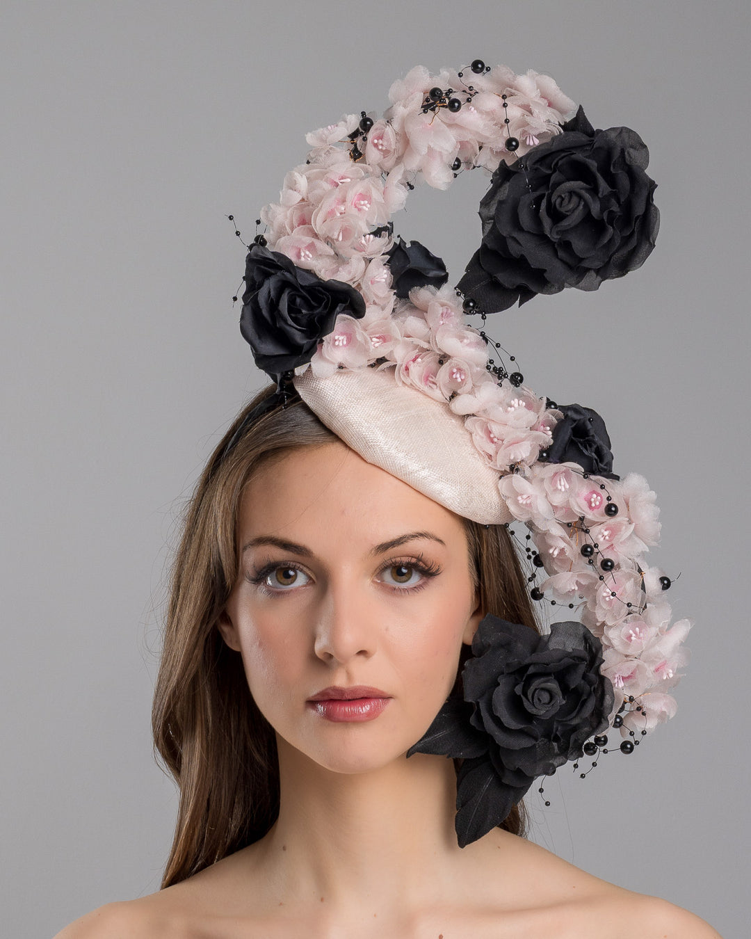 The model is showcasing the front side close up of the bush pink oval fascinator adorned with cascading black and soft pink chiffon flowers, accented with delicate black bead sprays, creating a dramatic, sculptural statement design. Designed and made by Merve Bayindir Millinery.