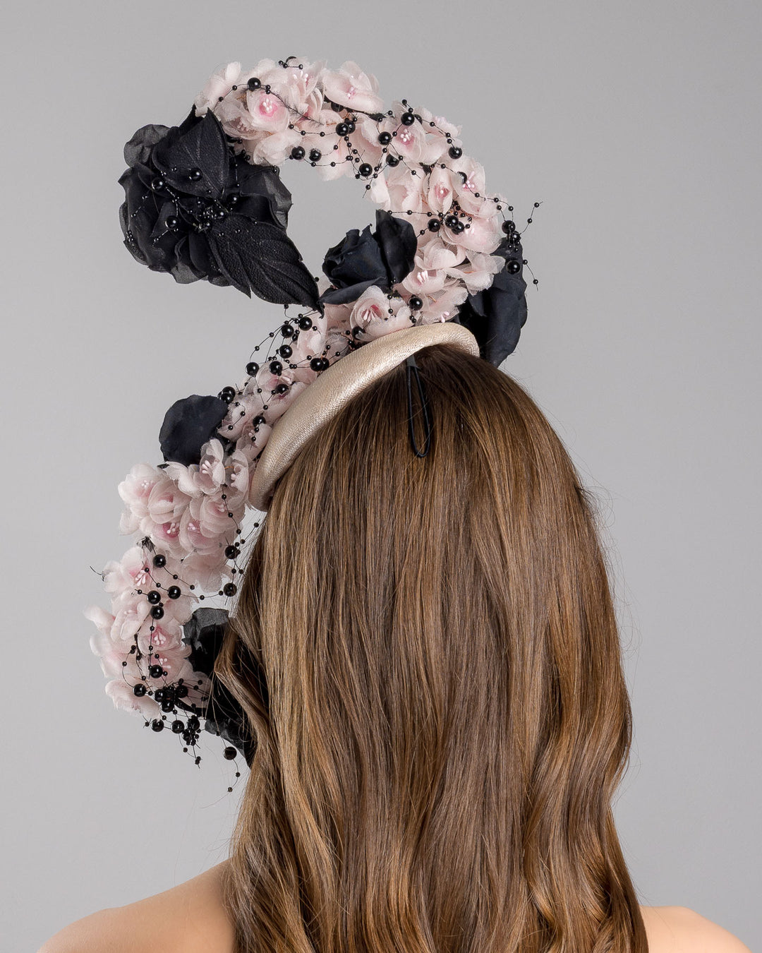 The model is showcasing the back side close up of the bush pink oval fascinator adorned with cascading black and soft pink chiffon flowers, accented with delicate black bead sprays, creating a dramatic, sculptural statement design. Designed and made by Merve Bayindir Millinery.