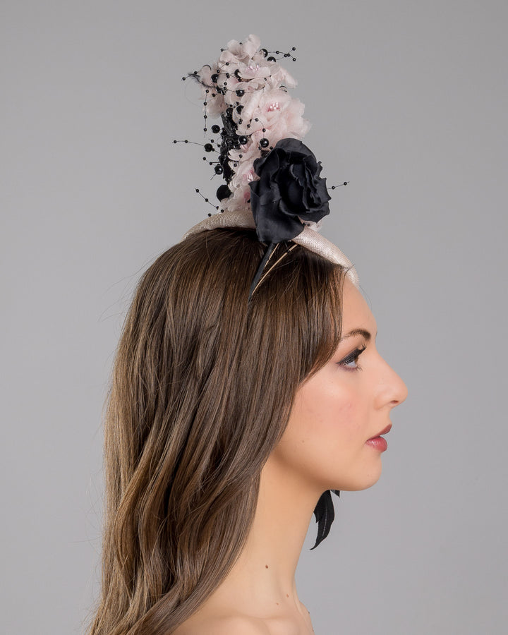 The model is showcasing the right side close up of the bush pink oval fascinator adorned with cascading black and soft pink chiffon flowers, accented with delicate black bead sprays, creating a dramatic, sculptural statement design. Designed and made by Merve Bayindir Millinery.