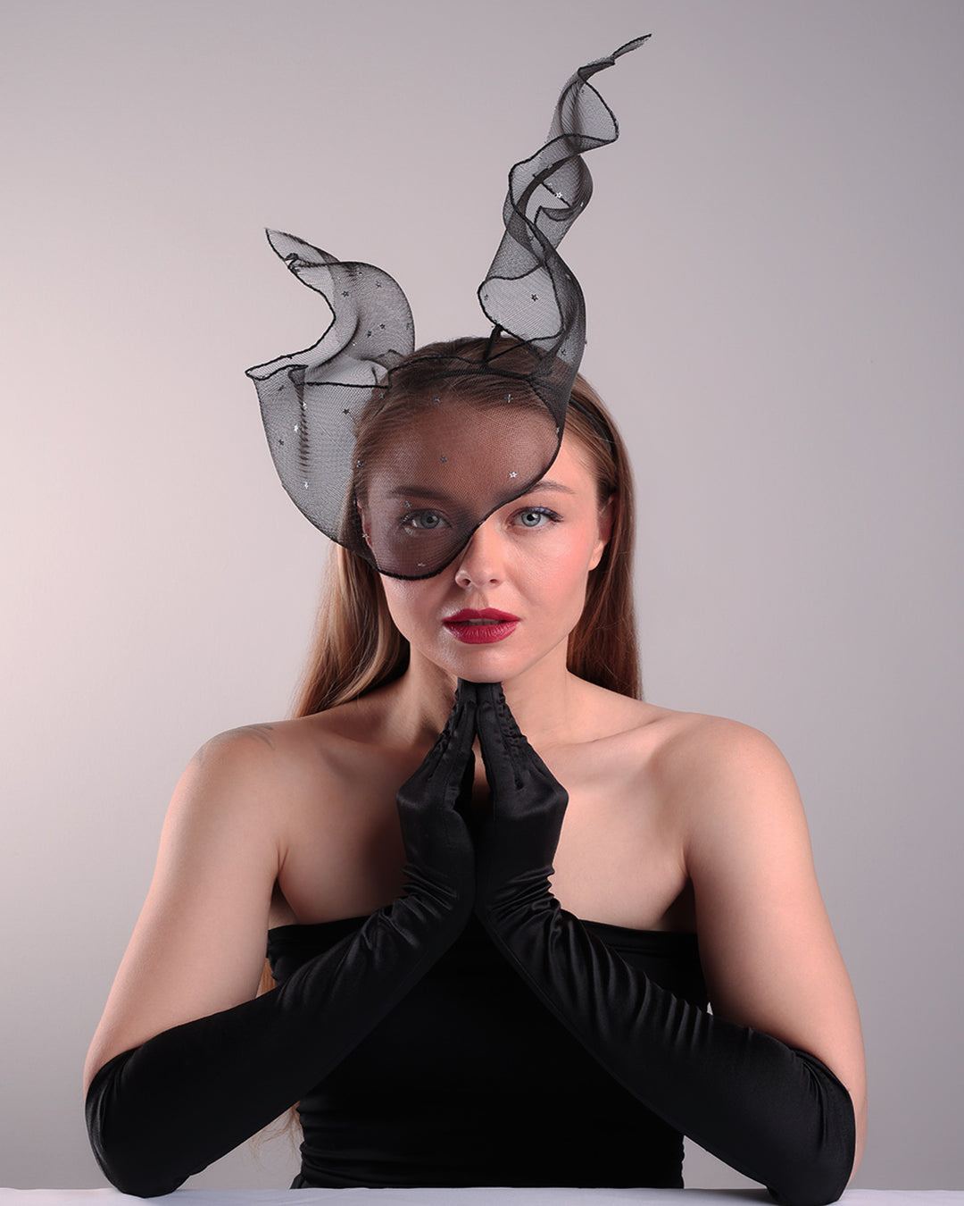 Model is showcasing the front view of the black crinoline, decorated with silver coloured star sequins, is wired and asymmetrically placed on a custom headband covering half of the face creating an illusion of a flying ribbon.