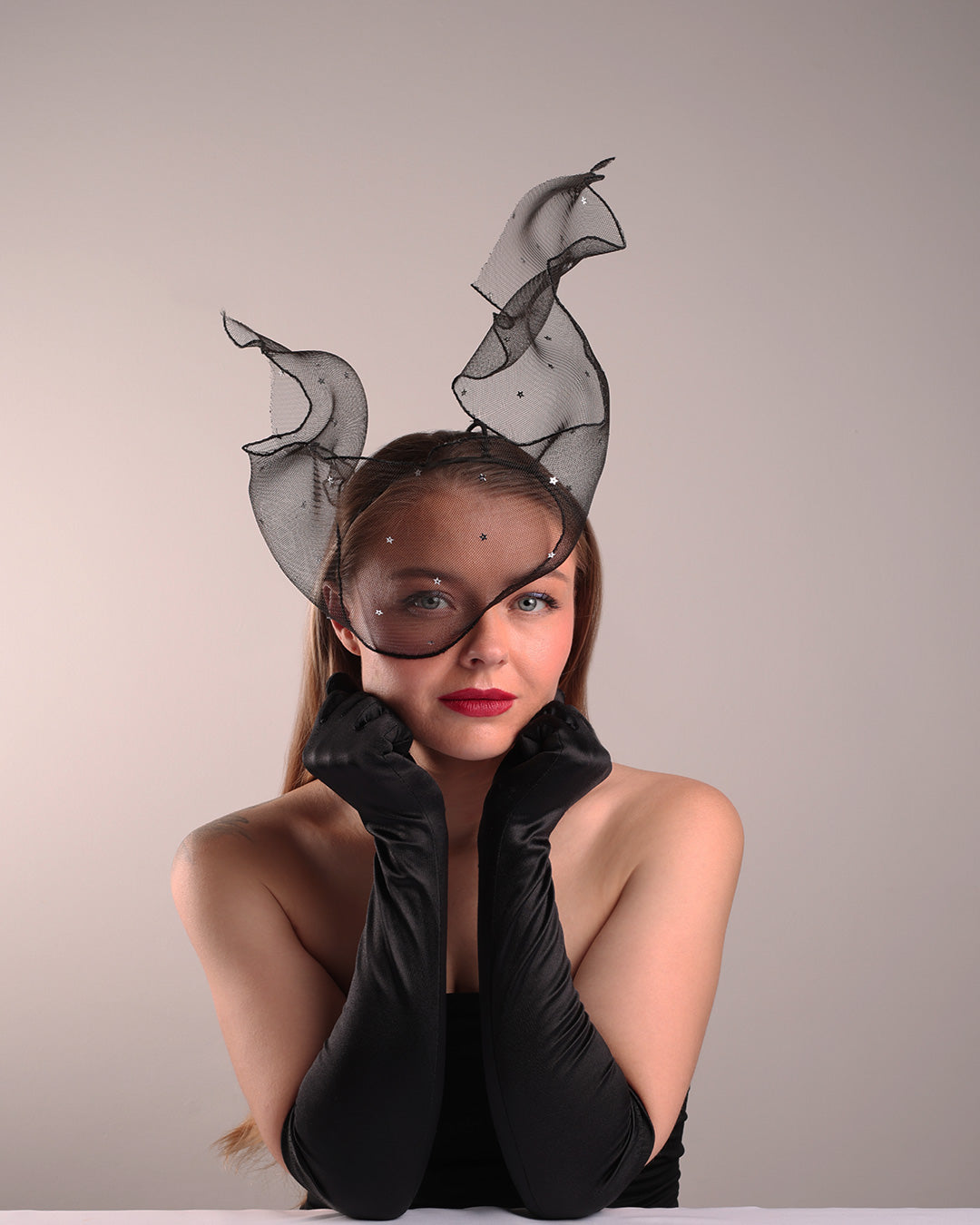 Model is showcasing the front right view of the black crinoline, decorated with silver coloured star sequins, is wired and asymmetrically placed on a custom headband covering half of the face creating an illusion of a flying ribbon.