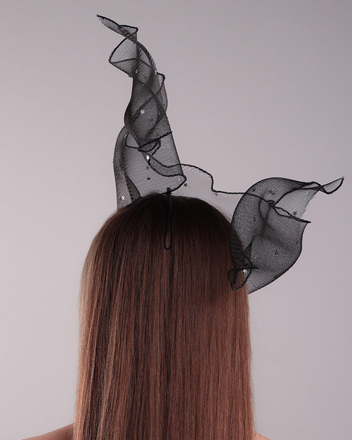 Model is showcasing the back side of the black crinoline, decorated with silver coloured star sequins, is wired and asymmetrically placed on a custom headband covering half of the face creating an illusion of a flying ribbon.