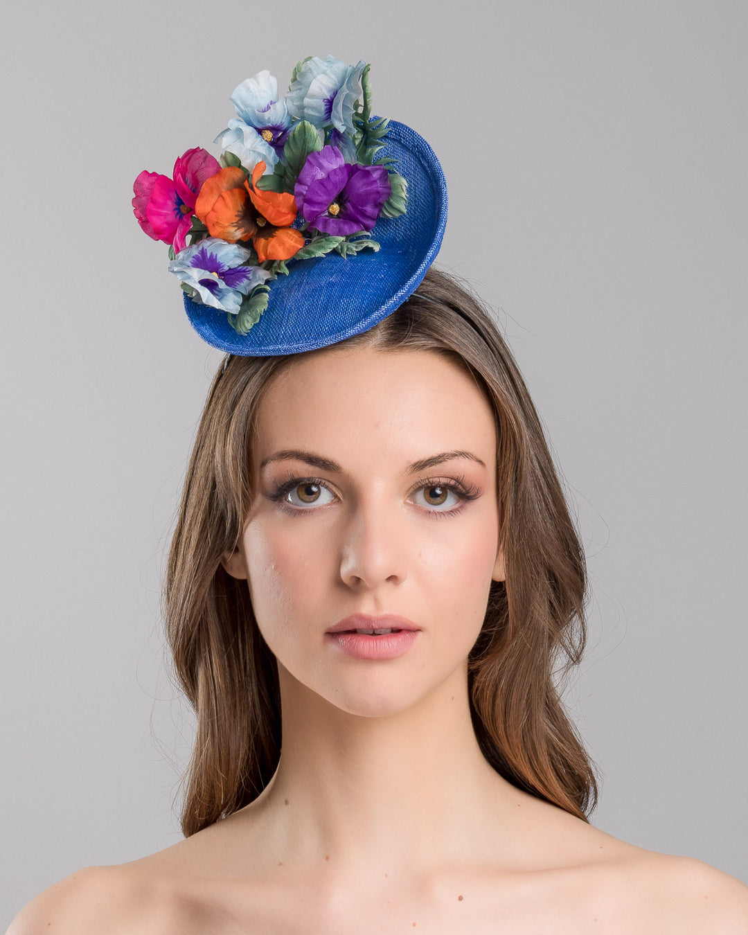 The model is showcasing the front side close up of the deep blue saucer style mini fascinator, decorate with different coloured violet flowers. Designed and made by Merve Bayindir Millinery.
