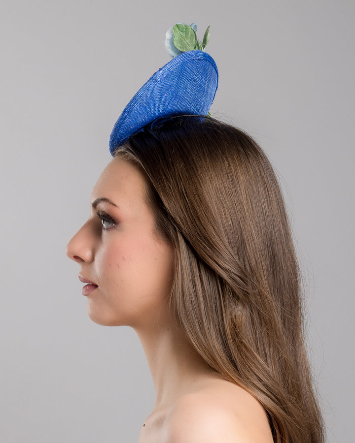 The model is showcasing the left side close up of the deep blue saucer style mini fascinator, decorate with different coloured violet flowers. Designed and made by Merve Bayindir Millinery.
