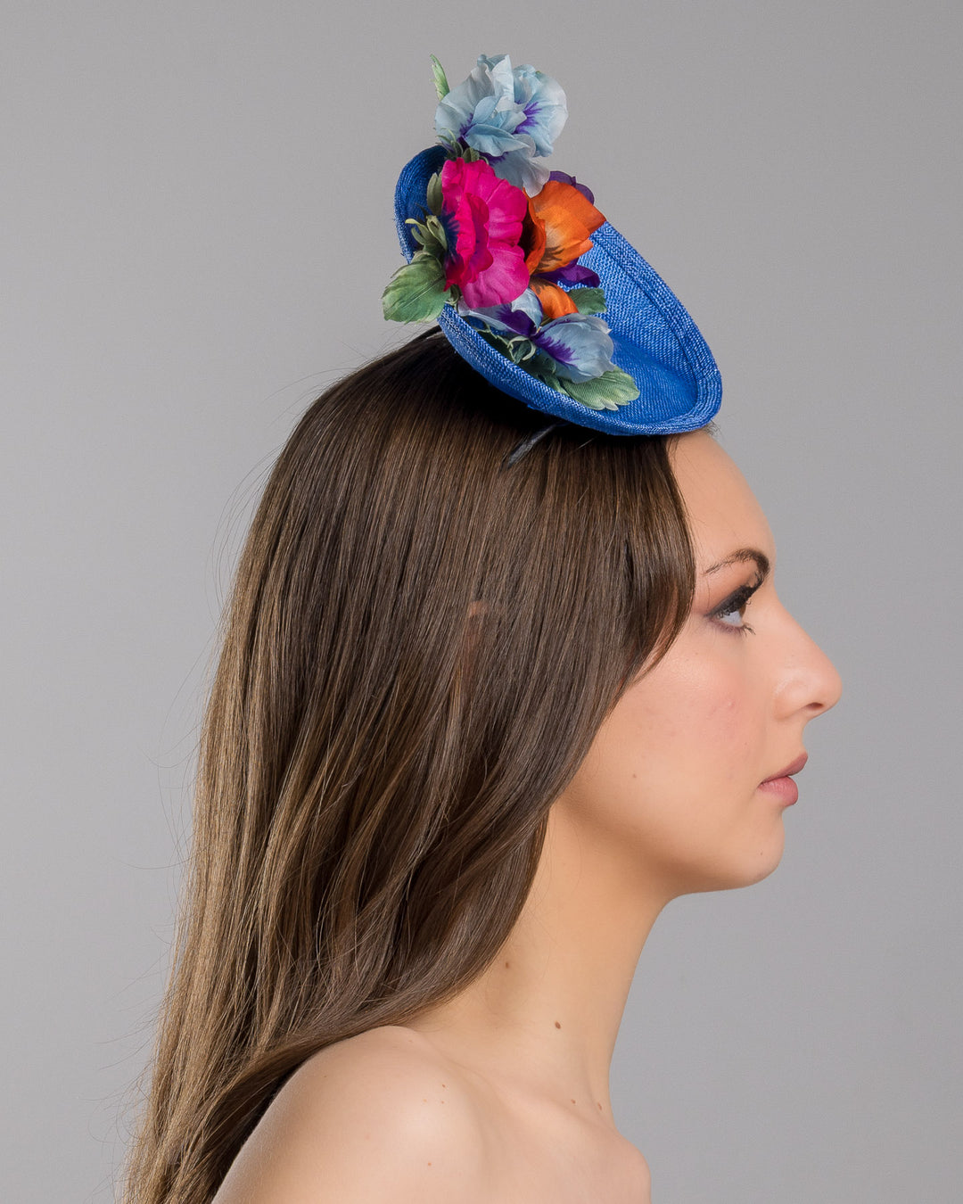 The model is showcasing the right side close up of the deep blue saucer style mini fascinator, decorate with different coloured violet flowers. Designed and made by Merve Bayindir Millinery.
