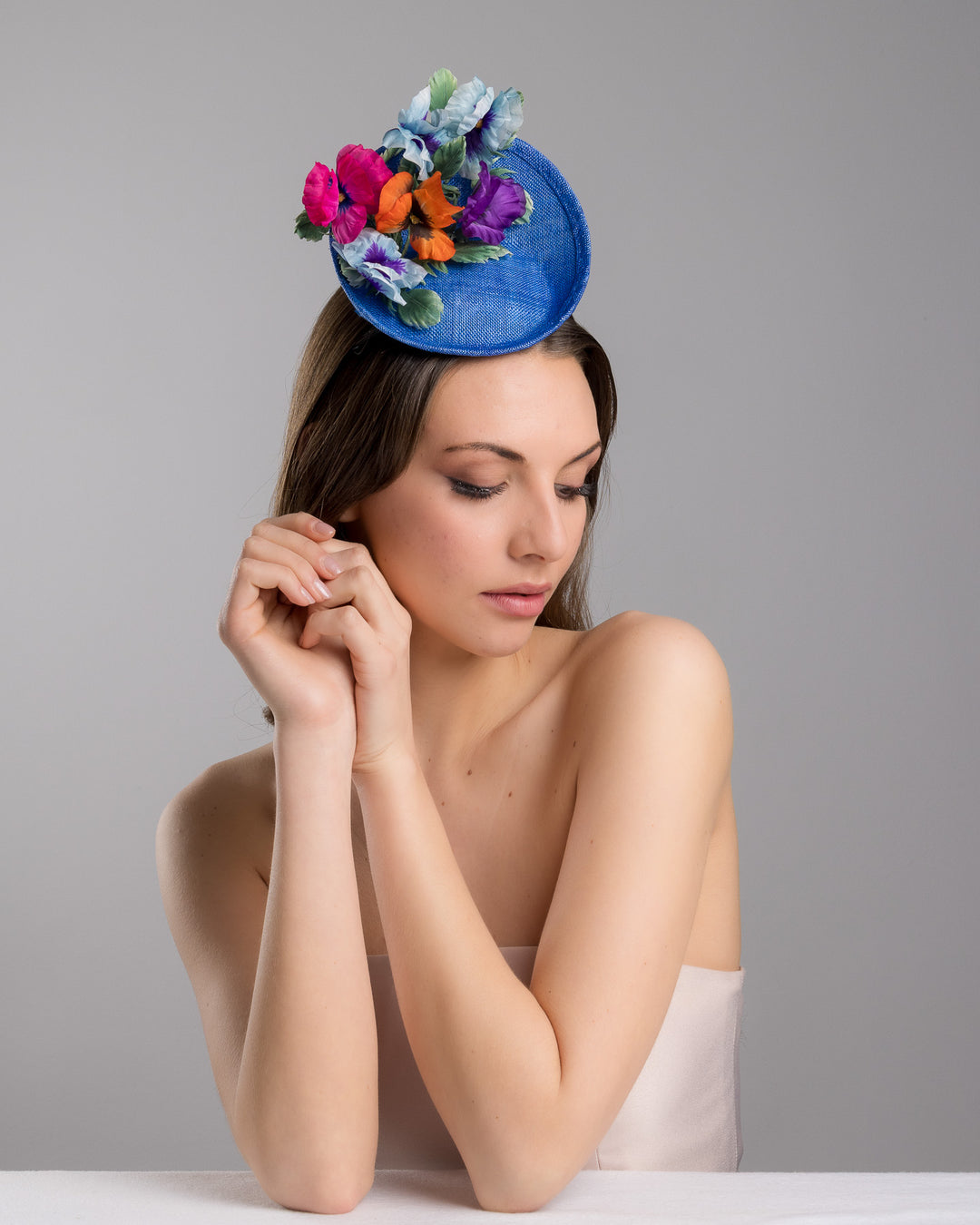 The female model is posing, wearing Shawn, the deep blue saucer style mini fascinator, decorate with different coloured violet flowers. Designed and made by Merve Bayindir Millinery.
