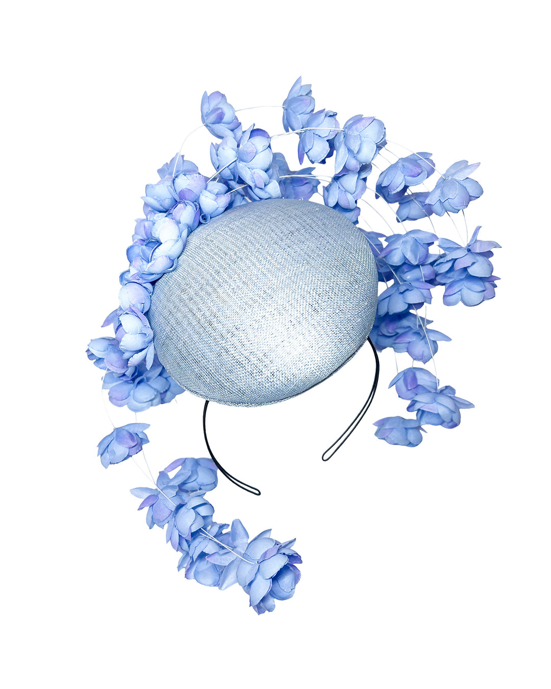 Light blue sinamay base fascinator with a softly domed shape and high back, adorned with clusters of delicate periwinkle-blue flowers that cascade outward on fine curved stems for an airy, sculptural effect. Designed and made by Merve Bayindir Millinery.

