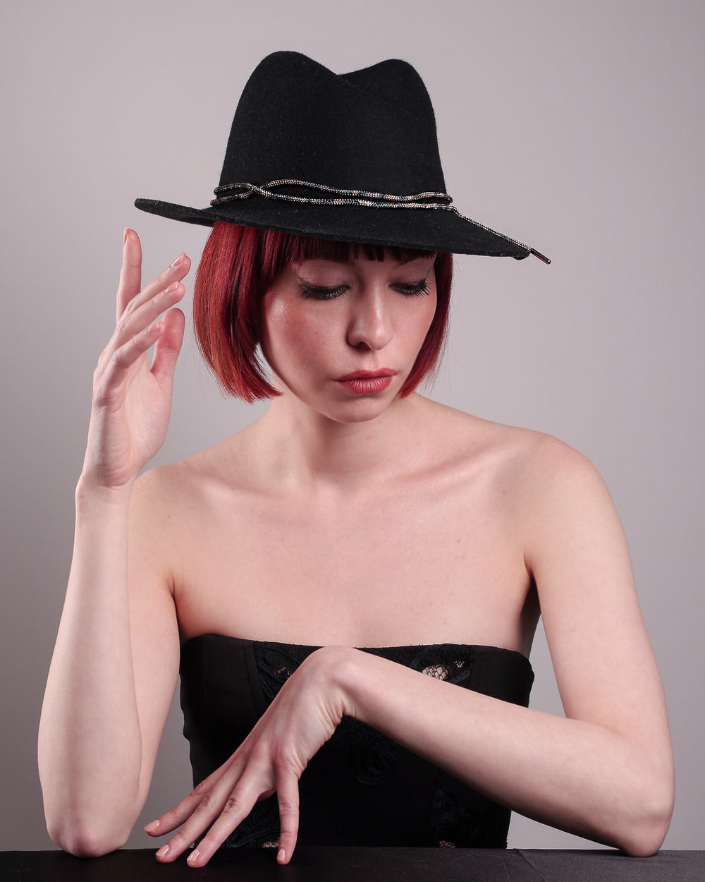 The model showcases the front of the Stella fedora crafted in deep black felt, the silhouette is elevated by a subtle metallic crystal band featuring strands of crystal embellished thread that catch the light with every tilt of the head. The tied ends fall just off-centre on the left side. Designed by Merve Bayindir.