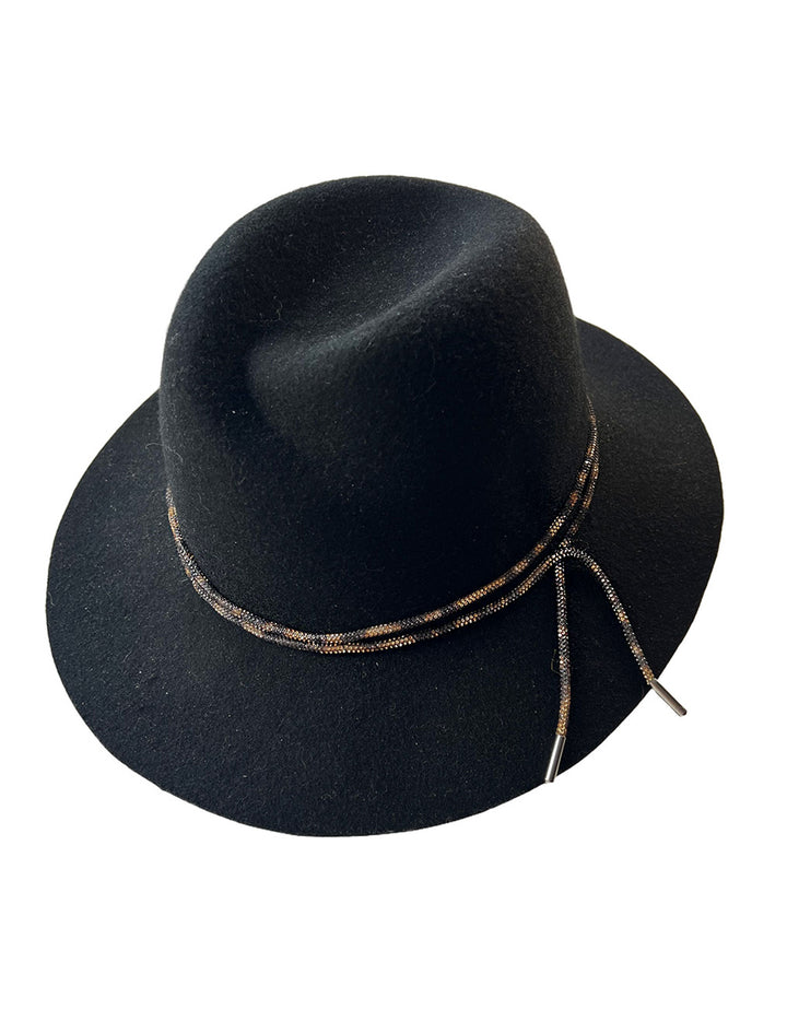 Still life picture of the Stella fedora crafted in deep black felt, the silhouette is elevated by a subtle metallic crystal band featuring strands of crystal embellished thread that catch the light with every tilt of the head. The tied ends fall just off-centre on the left side. Designed by Merve Bayindir.
