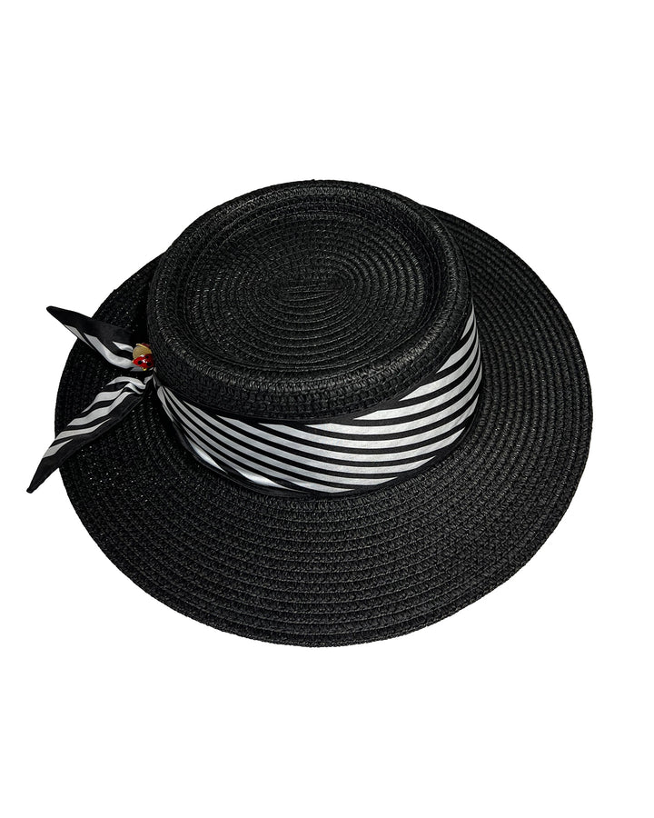 The picture showcases black woven straw boater hat with wide brim, finished with a black and white diagonal striped ribbon and a small red ladybug embellishment on the side. Designed and made by Merve Bayindir millinery.