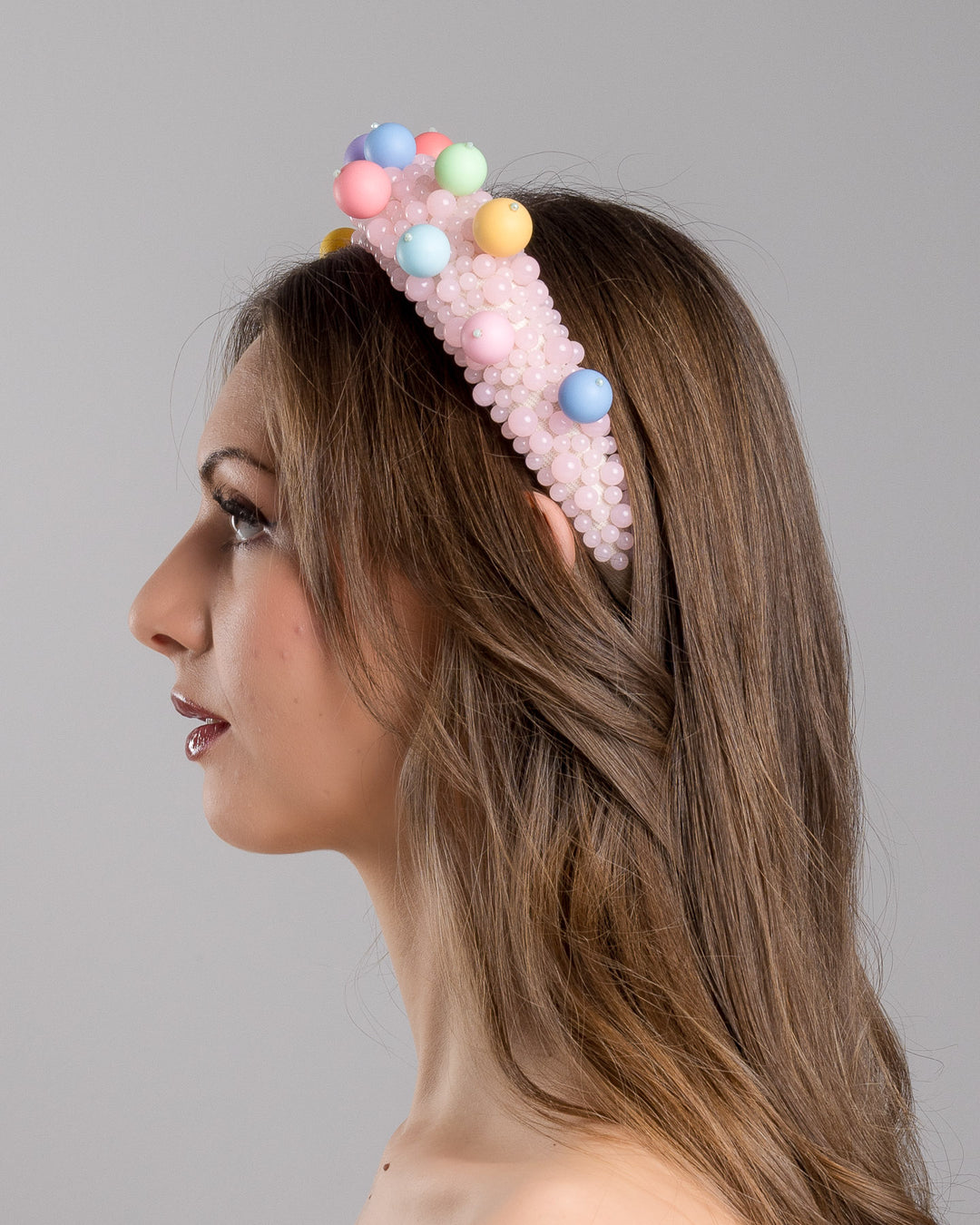 Model is showcasing left side close up multi size pink beaded headband adorned with large multi size mat bubble look a like multi colour multi size beads. Mde by Merve Bayindir.