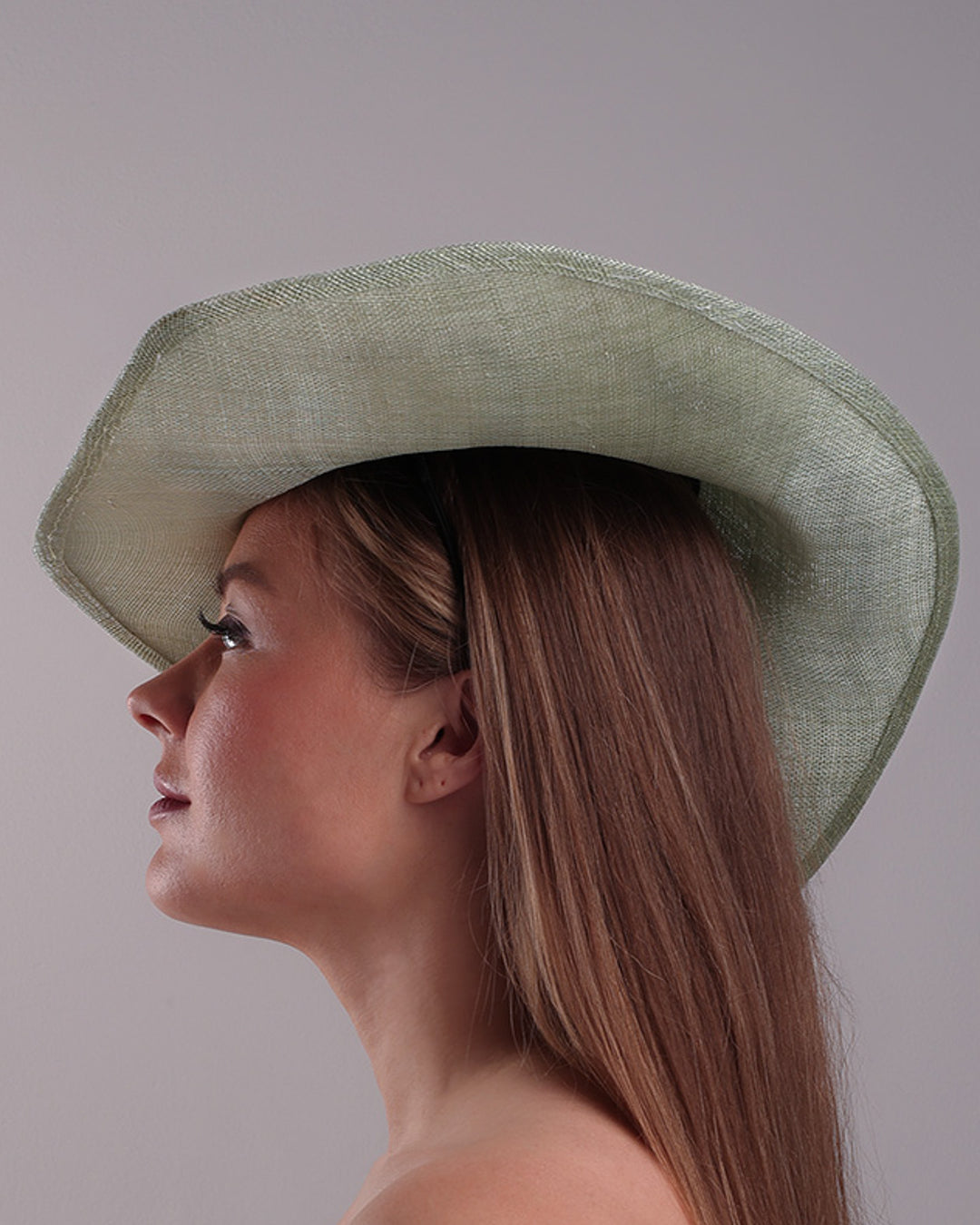 Model is showcasing the left side of green wide brim long hat, tilted to the right side swings upwards to the lefts side with a curve. Front top right side of the hat is decorated with multi colour resin flowers. Fitted to the head with wire headband and elastic.