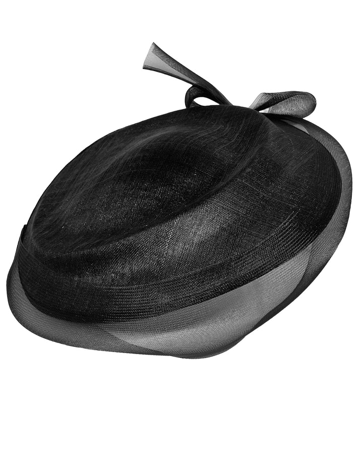 Black structured pillbox hat crafted from a grade sinamay, featuring a soft sheer veil overlay that drapes around the base and a delicate bow detail at the back. Designed and made by Merve Bayindir Millinery.


