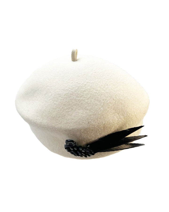 Still life picture of the Swan Felt Beret Hat, crafted from soft white felt and structured to sit perched to the side. A sculpted black swan with rhinestones glides outward in layers, featuring fan-like leather feathers at the end, which elegantly contrast with the creamy white base. Designed by Merve Bayindir.