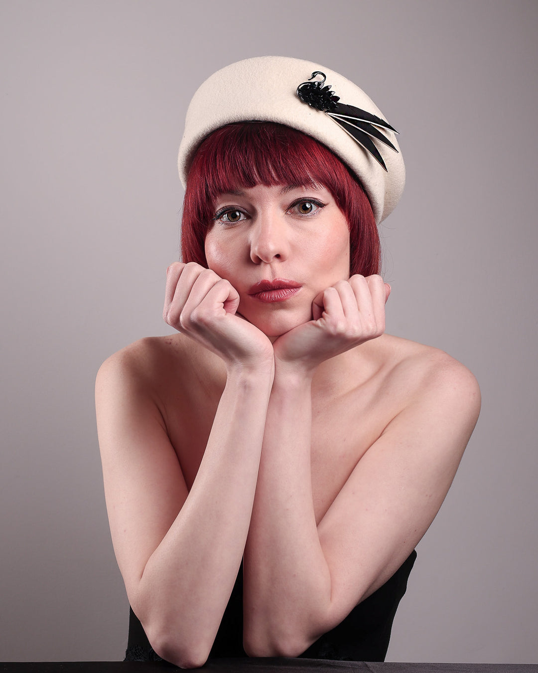 The model showcases the front of the Swan Felt Beret Hat, crafted from soft white felt and structured to sit perched to the side. A sculpted black swan with rhinestones glides outward in layers, featuring fan-like leather feathers at the end, which elegantly contrast with the creamy white base. Designed by Merve Bayindir.