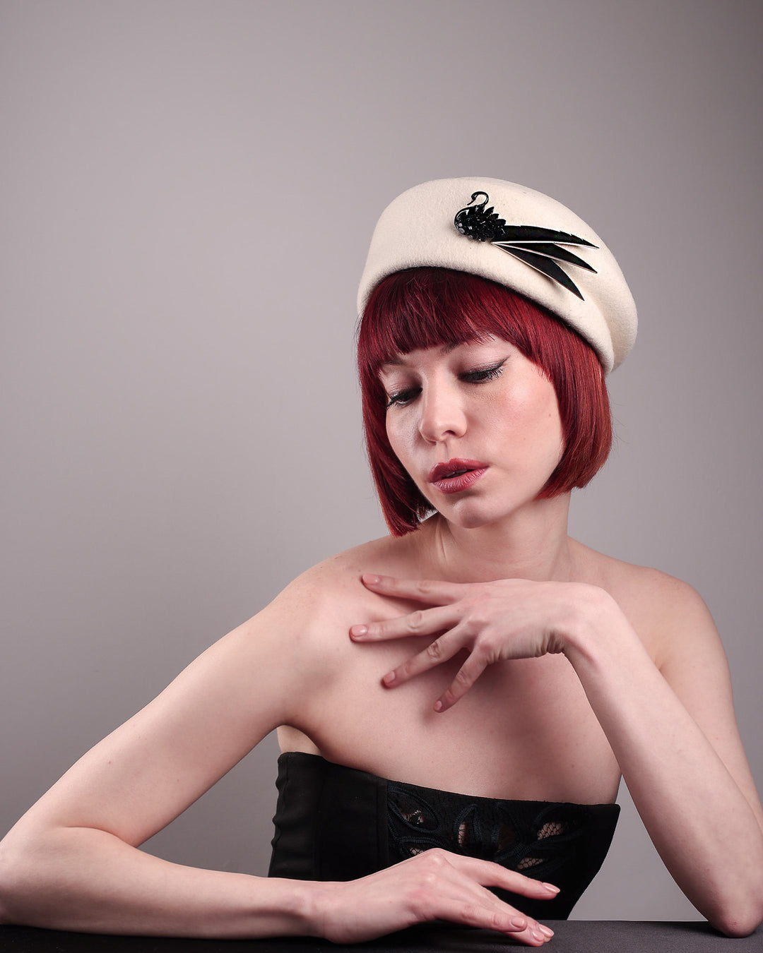 The model showcases the right front of the Swan Felt Beret Hat, crafted from soft white felt and structured to sit perched to the side. A sculpted black swan with rhinestones glides outward in layers, featuring fan-like leather feathers at the end, which elegantly contrast with the creamy white base. Designed by Merve Bayindir.