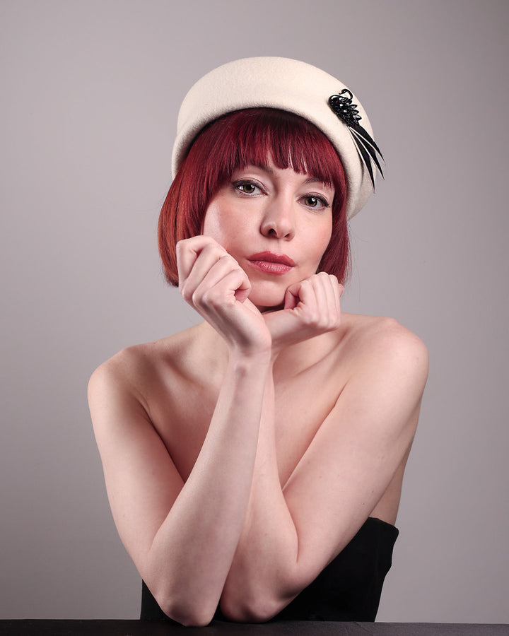 The model showcases the left front of the Swan Felt Beret Hat, crafted from soft white felt and structured to sit perched to the side. A sculpted black swan with rhinestones glides outward in layers, featuring fan-like leather feathers at the end, which elegantly contrast with the creamy white base. Designed by Merve Bayindir.
