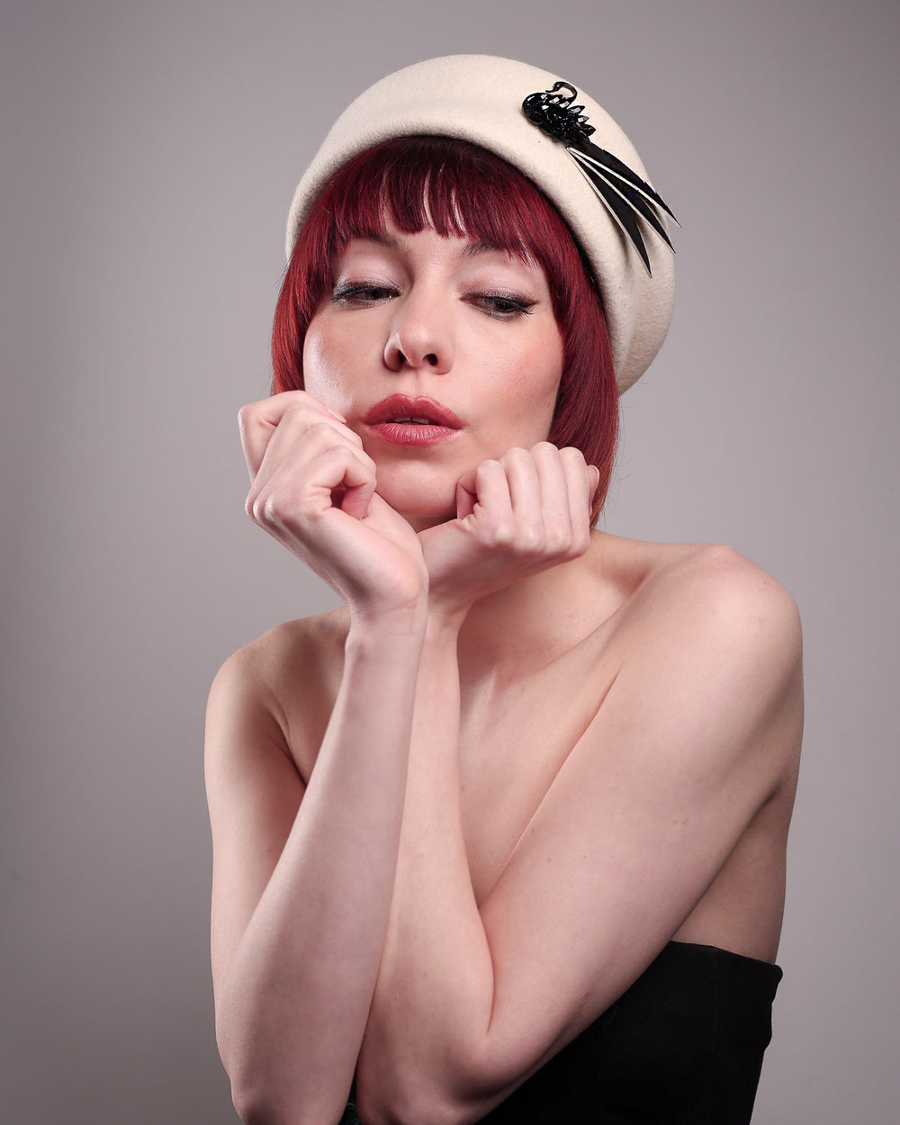 The model showcases the front of the Swan Felt Beret Hat, crafted from soft white felt and structured to sit perched to the side. A sculpted black swan with rhinestones glides outward in layers, featuring fan-like leather feathers at the end, which elegantly contrast with the creamy white base. Designed by Merve Bayindir.