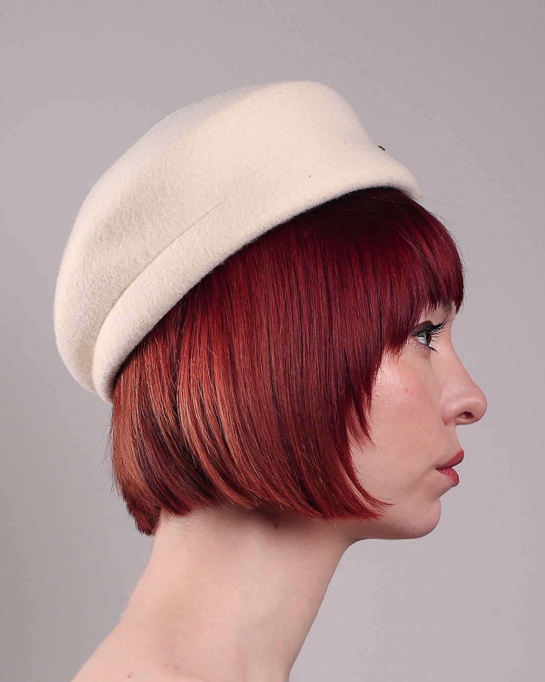 The model showcases theright side close up of the Swan Felt Beret Hat, crafted from soft white felt and structured to sit perched to the side. A sculpted black swan with rhinestones glides outward in layers, featuring fan-like leather feathers at the end, which elegantly contrast with the creamy white base. Designed by Merve Bayindir.