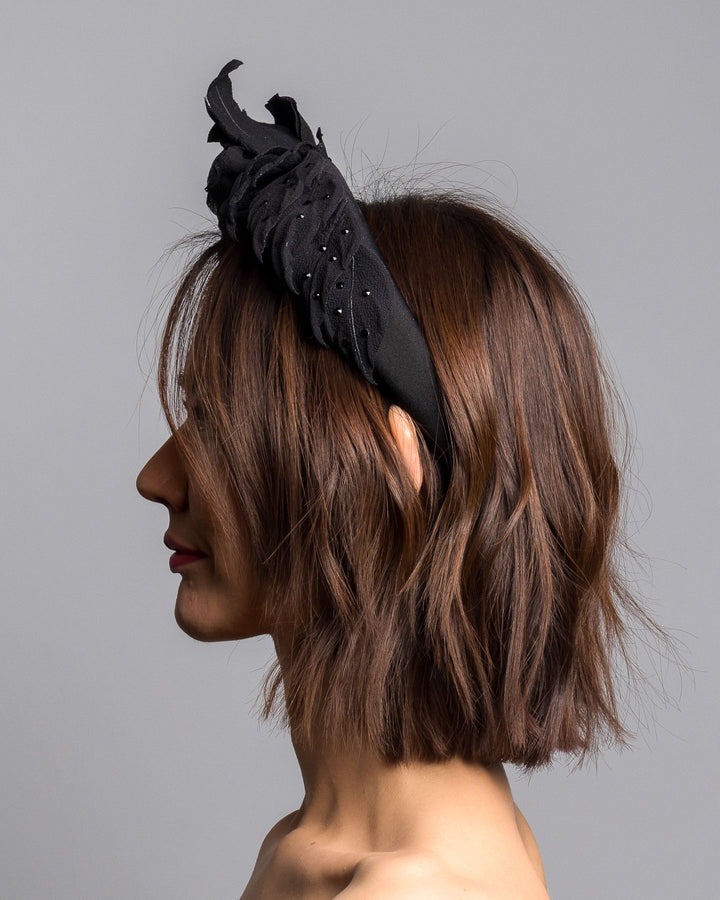 Model is showcasing the left side close up side of high lycra black headband, decorated with crepe rose and leafs embellished with crystals made by Merve Bayindir millinery.