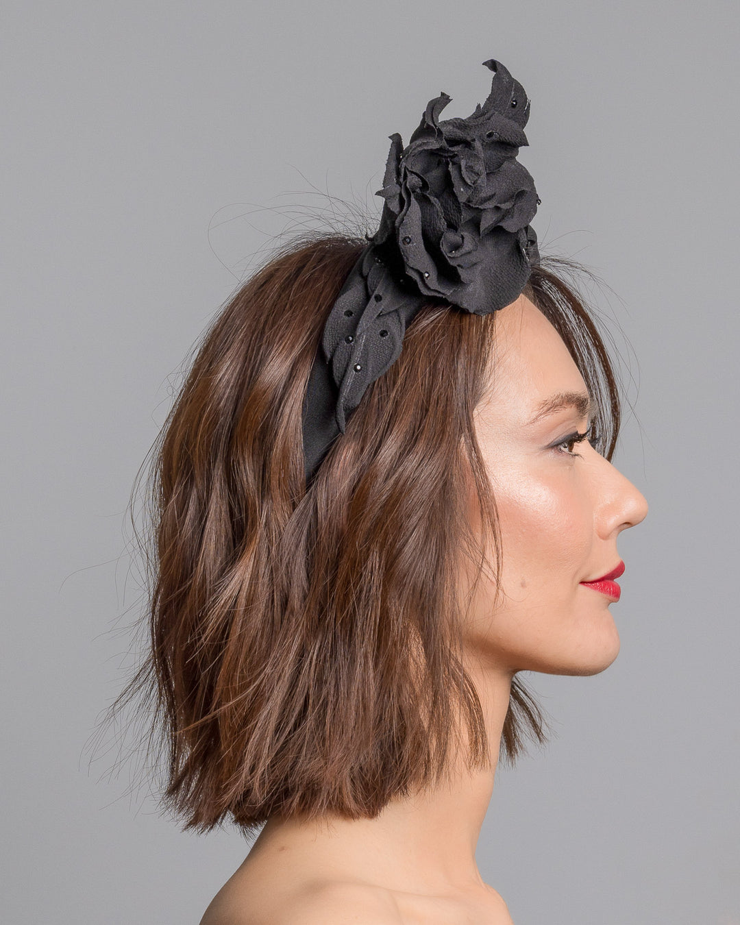 Model is showcasing the right side close up side of high lycra black headband, decorated with crepe rose and leafs embellished with crystals made by Merve Bayindir millinery.