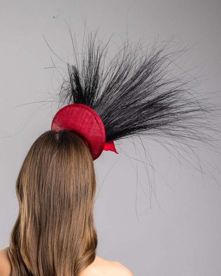 Model is showcasing the back side close up of mini red saucer fascinator, adorned with a red rose embellished with high rising black burnt peacock feathers. Designed and made by Merve Bayindir millinery.