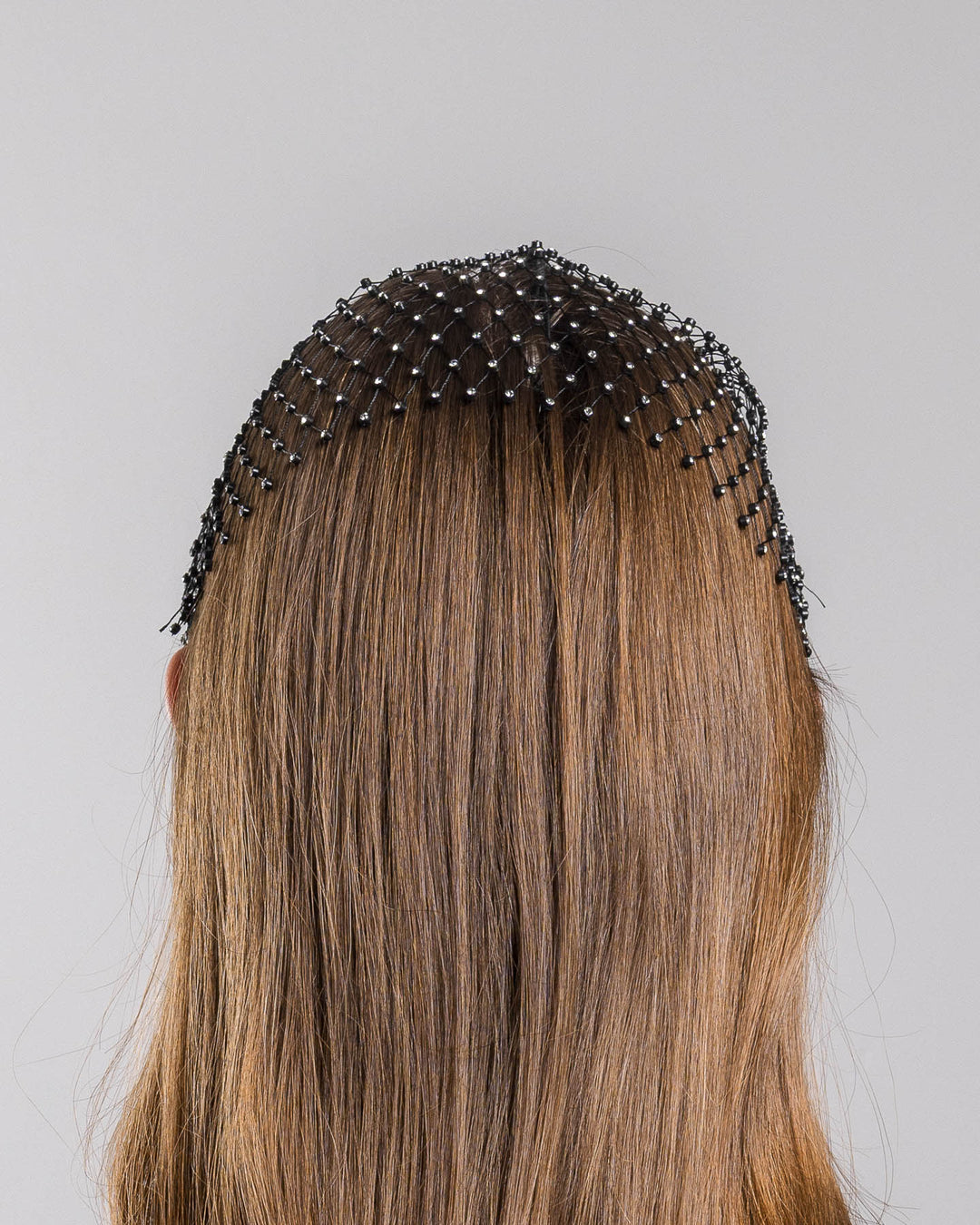The model is showcasing the back side close up of the black birdcage veil mask crafted from fine netting, embellished with a grid of small silver crystal accents and trimmed with delicate beaded edging for a dramatic, couture-inspired finish. Designed and made by Merve Bayindir Millinery.