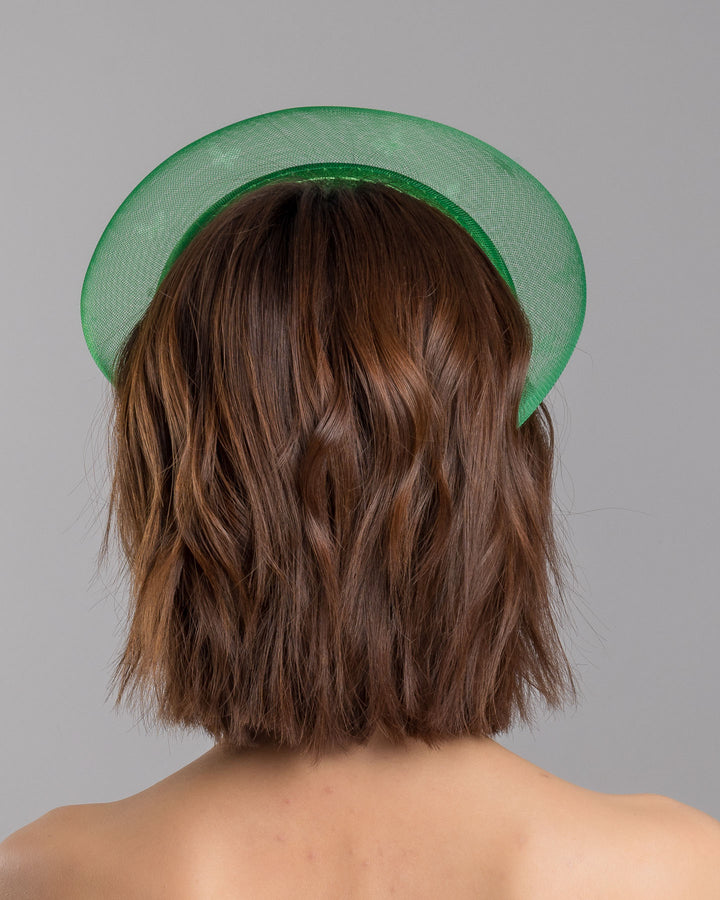 The model is showcasing the back side close up of the emerald green headband fascinator with a satin-covered base encircled by a sheer structured halo, decorated with small white butterfly appliqués for contrast and texture. Designed and made by Merve Bayindir Millinery.
