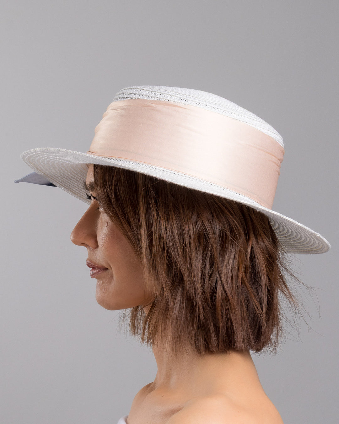 The model is showcasing the left side close up of the white woven straw boater hat with a wide brim, wrapped in a soft beige silk ribbon and finished with a tied scarf featuring illustrated panda motifs at the side. Designed and Made by Merve Bayindir millinery