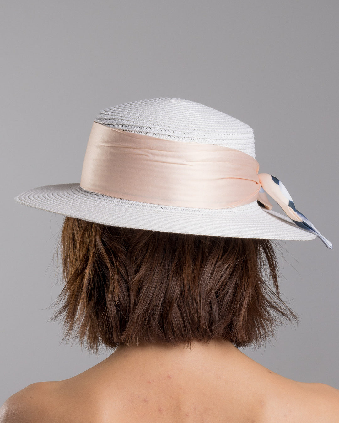 The model is showcasing the back side close up of the white woven straw boater hat with a wide brim, wrapped in a soft beige silk ribbon and finished with a tied scarf featuring illustrated panda motifs at the side. Designed and Made by Merve Bayindir millinery