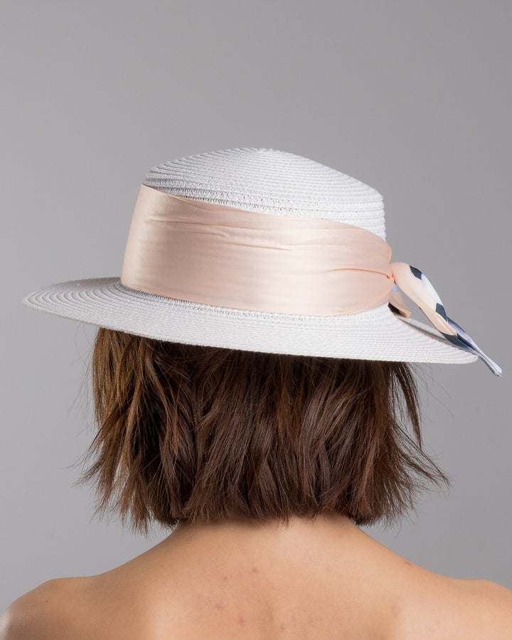 The model is showcasing the back side close up of the white woven straw boater hat with a wide brim, wrapped in a soft beige silk ribbon and finished with a tied scarf featuring illustrated panda motifs at the side. Designed and Made by Merve Bayindir millinery