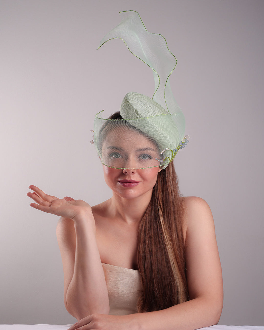 Model is showcasing thefront of light grean tear drop fascinator moving from the top right of the face to the left cheek. The beautiful fascinator adorned with a scultured crinoline that covers the eyes in veil llike position and fly from side to back high creating a wind flown shawl effect. Both sides of the crinoline piece is decorated with bead embroidery to give it a toucsh of softness.
