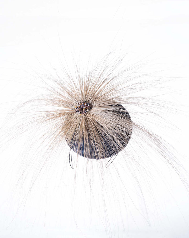 Still life picture of Navy coloured button shaped fascinator decorated with natural coloured burnt extra long peacock feathers and cluster of crystals. Made by Merve Baindir millinery.