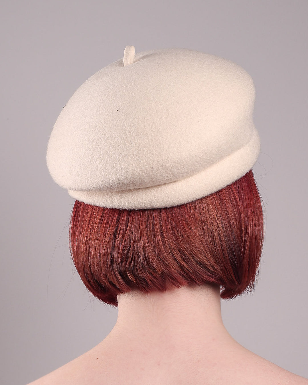 The model, showcasing the back of the Vitra Beret, crafted from soft white felt, features a scattering of hand-applied black wire flowers on the front to left side that seem to dance across the crown like doodles. Designed by Merve Bayindir.