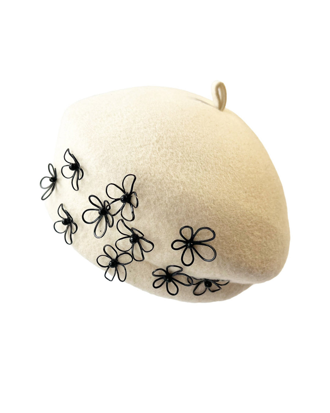 Still life picture of the Vitra Beret, crafted from soft white felt, features a scattering of hand-applied black wire flowers on the front to left side that seem to dance across the crown like doodles. Designed by Merve Bayindir.