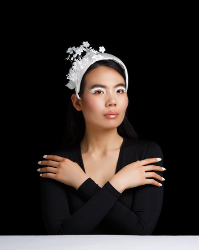 Model is featuring a Half moon style white hat decorated with sateen flowers on the right side with leaves.