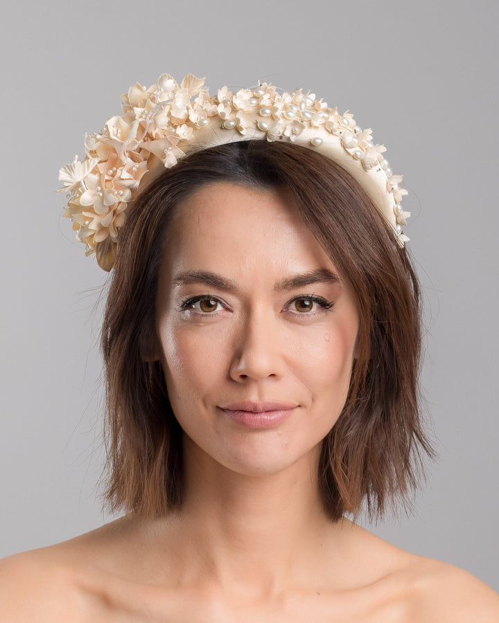 Model is showcasing the front side close up of beige coloured silk sateen ivory headband decorated with ivory cotton flowers an ivory beads. Made by Merve Bayindir.
