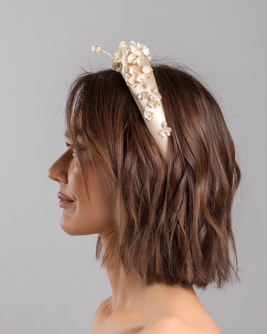 Model is showcasing the left side close up of beige coloured silk sateen ivory headband decorated with ivory cotton flowers an ivory beads. Made by Merve Bayindir.