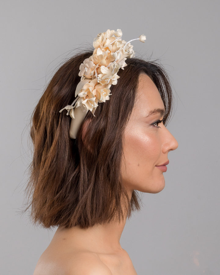 Model is showcasing the right side close up of beige coloured silk sateen ivory headband decorated with ivory cotton flowers an ivory beads. Made by Merve Bayindir.