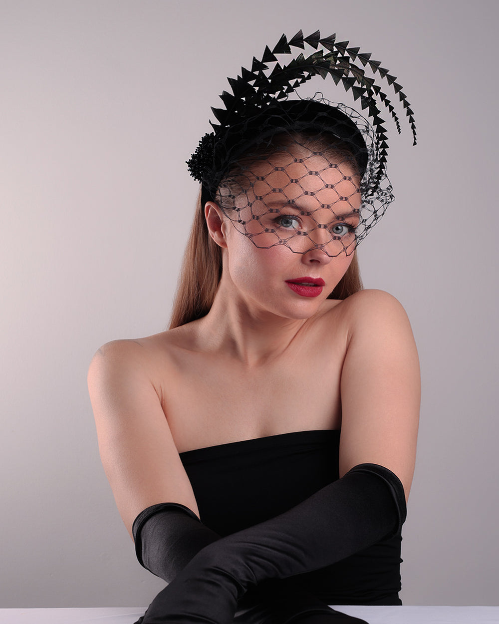 Model is showcasing the front right angle of the black velvet high headband is decorated with widdow style veil, adorned with custom trimmed black rooster feathers curving on top of the headband. The end of the feathers is embellished with black crystal cluster where they meet with the headband.