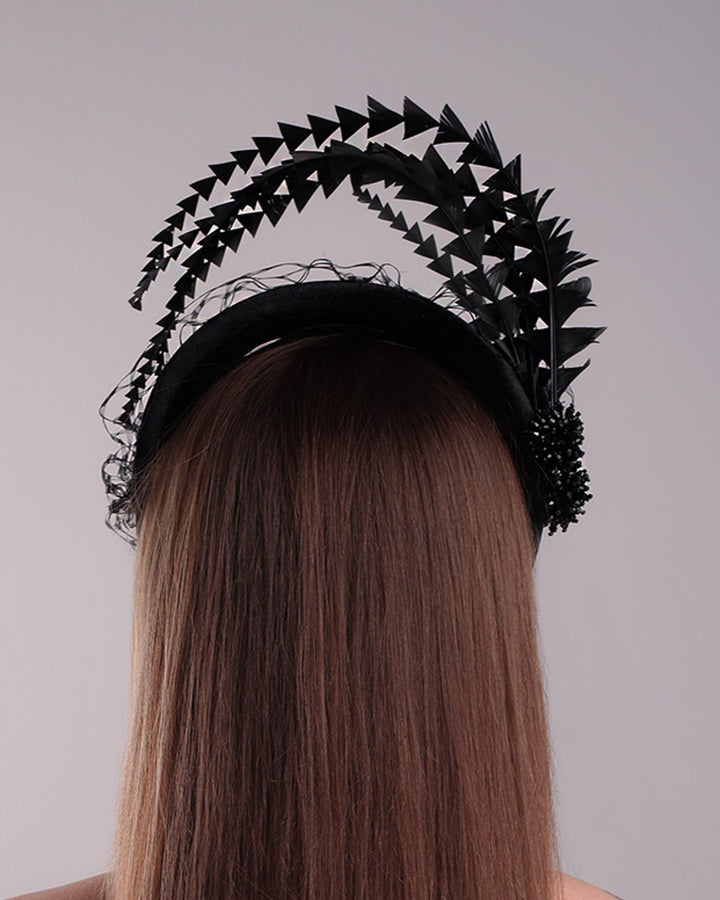 Model is showcasing the back side of the black velvet high headband is decorated with widdow style veil, adorned with custom trimmed black rooster feathers curving on top of the headband. The end of the feathers is embellished with black crystal cluster where they meet with the headband.