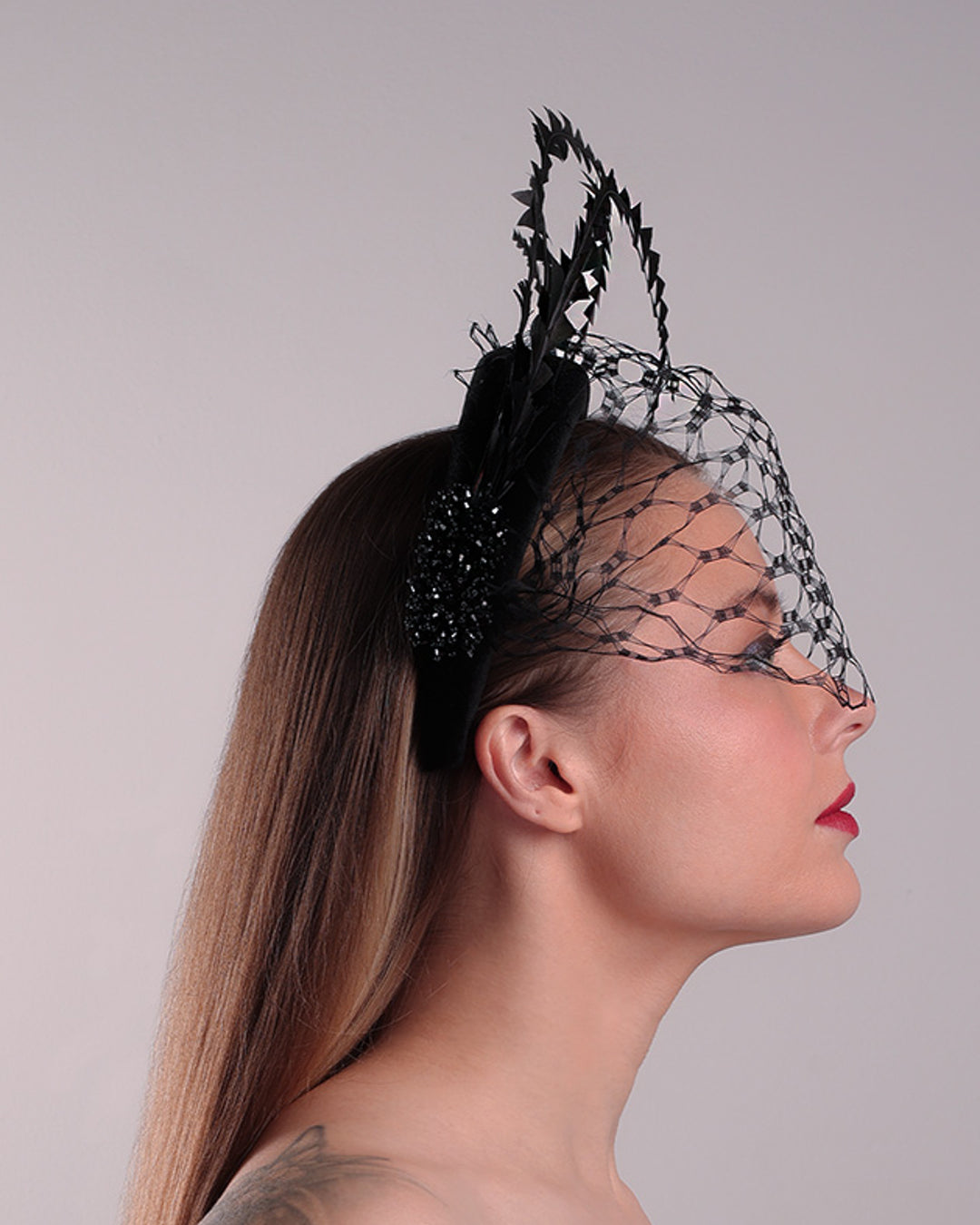 Model is showcasing the right side of the black velvet high headband is decorated with widdow style veil, adorned with custom trimmed black rooster feathers curving on top of the headband. The end of the feathers is embellished with black crystal cluster where they meet with the headband.
