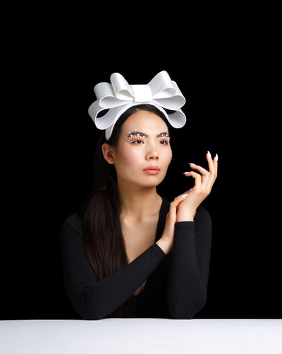 Model is showcasing a Three silk saten bows, three sizes placed like a pyramid giving the illusion of hight with the most elegant way on a custom made headband.