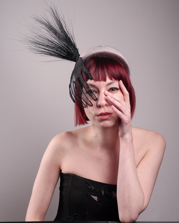 The model showcases the front of the Zephyr grey velvet headband with the hand-shaped wire black glove fitted with crinoline cascades dramatically across the face, balanced by a bursting spray of sleek horsehair. Designed by Merve Bayindir.